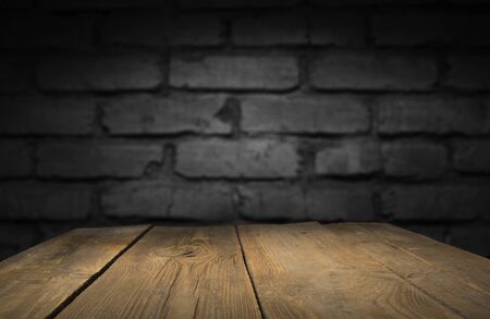 Old wood table with blurred concrete block wall in dark room background.