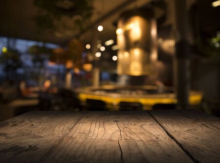 Empty wood table top on blur light gold bokeh of cafe restaurant in dark background.の写真素材