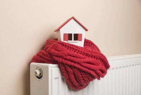 house in winter - heating system concept and cold snowy weather with model of a house wearing a knitted capの写真素材