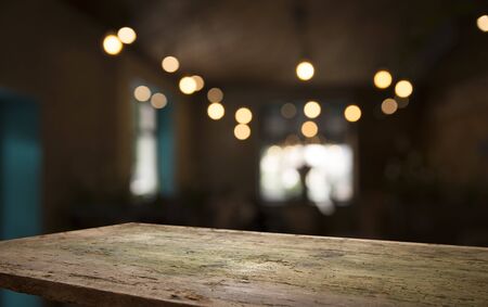 Empty wood table top on blur light gold bokeh of cafe restaurant in dark background.