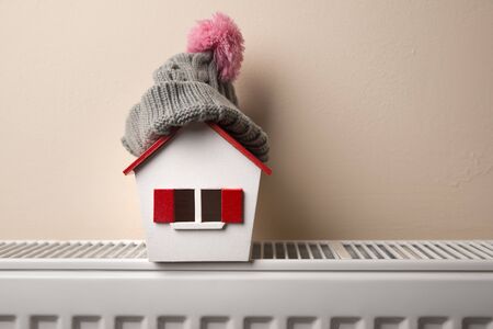 house in winter - heating system concept and cold snowy weather with model of a house wearing a knitted capの写真素材