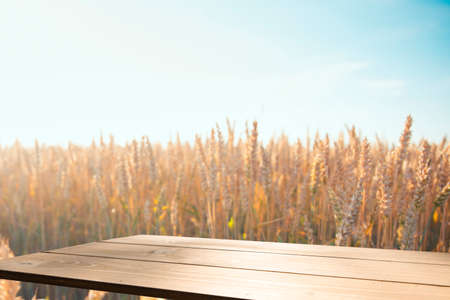 Empty wooden deck table over wheat field with sunset or sunrise. Ready for product montageの写真素材