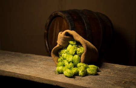 Beer. Still life with Vintage beer barrel and glass light beer. Fresh amber beer concept. Green hop and gold barley on wooden table. Ingredients for brewery. Brewing traditionsの写真素材