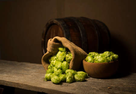 Beer. Still life with Vintage beer barrel and glass light beer. Fresh amber beer concept. Green hop and gold barley on wooden table. Ingredients for brewery. Brewing traditionsの写真素材