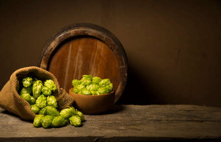 Beer. Still life with Vintage beer barrel and glass light beer. Fresh amber beer concept. Green hop and gold barley on wooden table. Ingredients for brewery. Brewing traditionsの写真素材