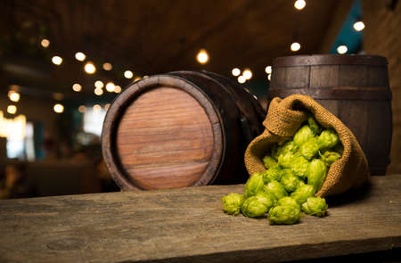 Beer. Still life with Vintage beer barrel and glass light beer. Fresh amber beer concept. Green hop and gold barley on wooden table. Ingredients for brewery. Brewing traditionsの写真素材