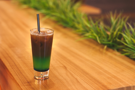 Ice coffee wich blue green cocktailcold coffee and green, blue syrup. Summer refreshing cocktail on wooden table in a coffee house, restaurant.の写真素材