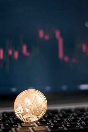 Golden Monero in front of laptop with stock exchange graph background. Digital money concept.の写真素材