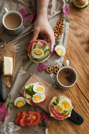 Toast with avocado, egg, tomatoes and cup of coffee. Healthy breakfast. Hands holding plate with healthy breakfast food. Concept of healthy lifestyleの写真素材