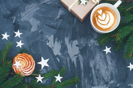 Christmas cake with white ceramic cup of cappuccino and gift box on black background. White xmas star and branches decorations on table. Copy space. Top view. Christmas concept.の写真素材