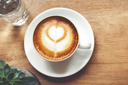Cup of cappuccino with latte art on wooden background with plant. Hot coffee with flower on table. Top view, flat lay copy space for text. Beautiful foam, top view, copy space.の写真素材