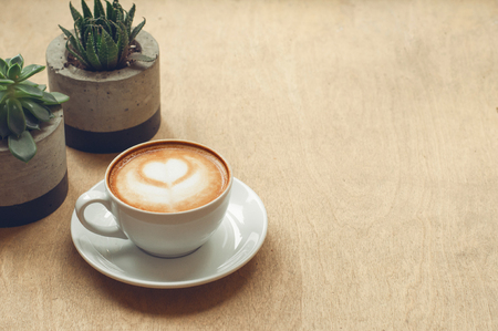Cup of cappuccino with latte art on wooden background with plant. Hot coffee with flower on table. Top view, flat lay copy space for text. Beautiful foam, top view, copy space.の写真素材