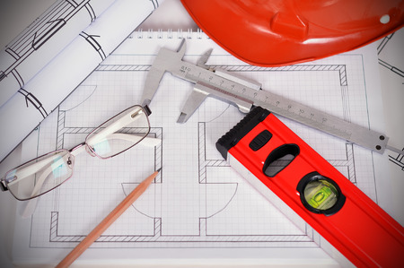 hard hat with blueprints, line level and caliper on table