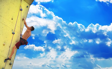 Young muscular man climbing on wall and blue skyの写真素材
