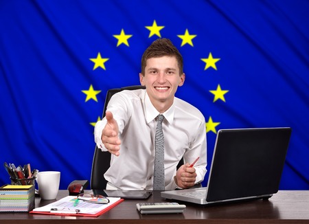 businessman sitting in office and reaches out on a European Union flag on backgroundの写真素材