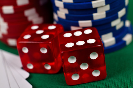 two red dice and poker chips on green table, close up