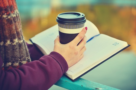 Female hands holding cup of coffee and book. Vintage photoの写真素材