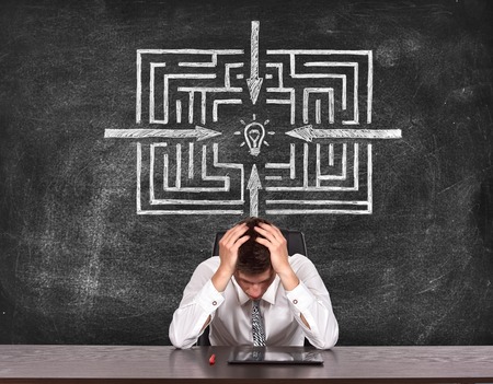 tired businessman sitting at table and drawing way to success on blackboardの写真素材