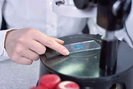 Laboratory worker examines a sample of a chemical through a microscopeの写真素材