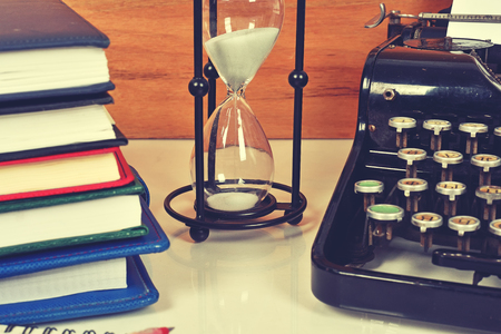 Hourglass, books and vintage typewriter on table  in vintage color toneの写真素材