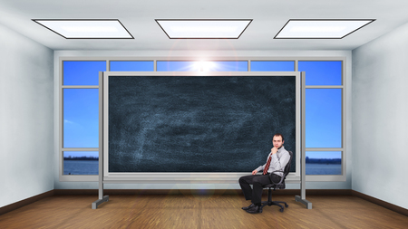 Businessman sitting in classroom. Blank chalk board.の写真素材