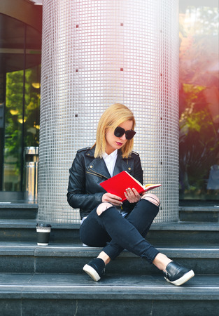 young hipster girl reading a red  book sitting on stairsの写真素材