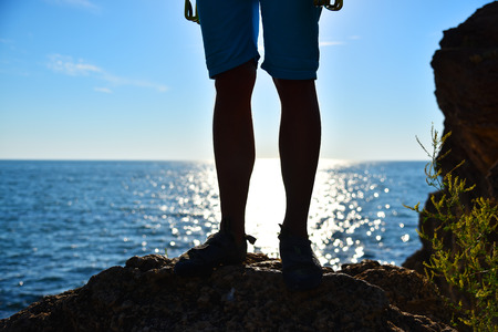 foot climber on a cliff, sunsen in ocean on backgroundの写真素材