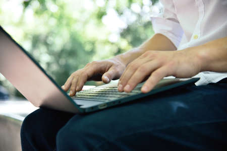 Student sitting in park and typing on laptop. Education and working concept. Close up