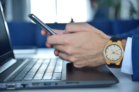 Businessman hands with wooden watch using smart phone. Technology and trade concept.