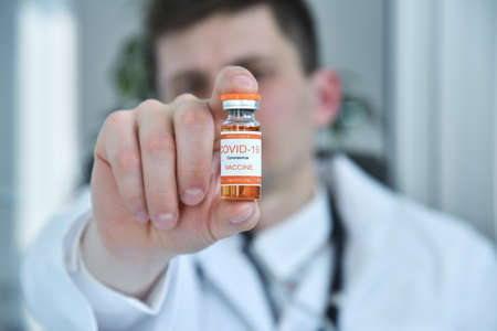 Doctor in clinic holding coronavirus vaccine in glass bottle in hand. Coronavirus Covid19 and...