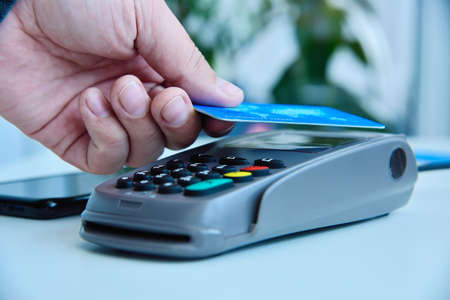 Hand customer holding blue credit card hear nfc pos terminal. Transaction pay and shopping concept.