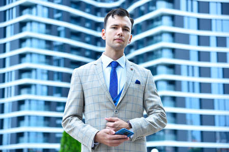 Businessman with mobile phone in hand on modern building background. Business and technology concept.の写真素材