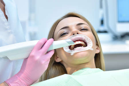 Woman dentist using dental intraoral scanner while examining patient teeth in dental clinic. Intraoral scanning with modern scanning machine concept.の写真素材