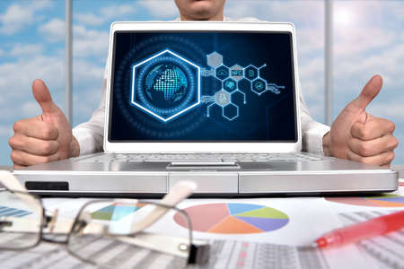 Businessman showing thumb and hexagons hologram with digital business icons on laptop screen....