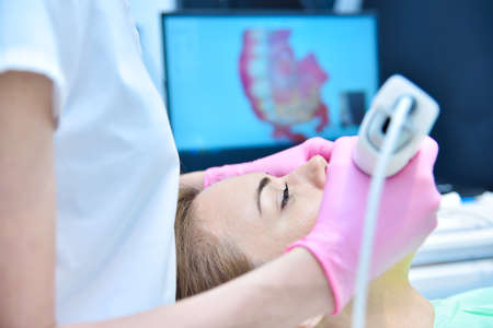 Dentist in pink gloves scaning patient's teeth with dental 3d scanner and laptop screen with 3d scanning of jaw. Healthcare and stomatology conceptの写真素材