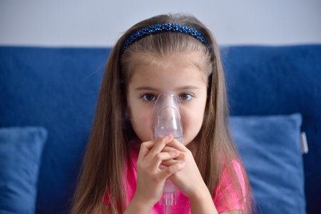 Close up of little girl with asthma inhaler at home. Health care and medical concept.の写真素材