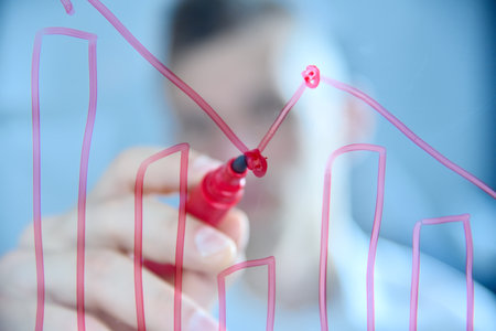 Businessman drawing bar graphs with red marker on transparent glass board, focusing on analysis and data. Concept of business analysis and data visualizationの写真素材