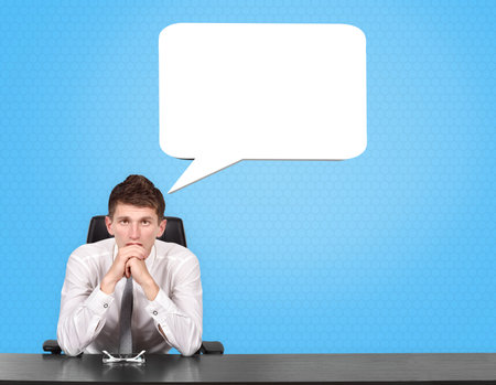 Businessman sitting at the desk and thinking with speech bubble over blue background. Concept of business analysisの写真素材