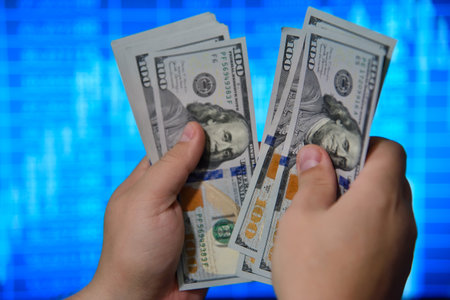 Businessman hands holding and counting dollar bills with a stock market chart background, symbolizing finance and investmentsの写真素材