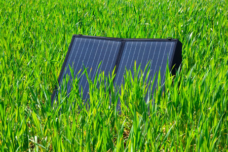 Foldable solar panel placed in tall green grass, natural lighting, eco-friendly energy concept, renewable power in outdoor settingの写真素材
