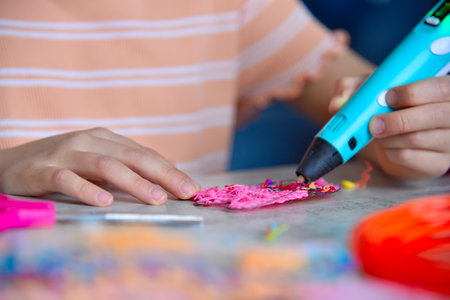 Girl hands creating plastic 3D model with 3d pen on paper at table. Concept of creativity and...