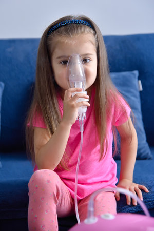 Little girl with pink pig inhaler on table at home. Health care and medical concept. Close upの写真素材