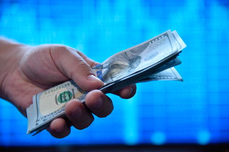 Hands holding and counting dollar banknotes with a stock chart background, symbolizing finance and investments. Close upの写真素材