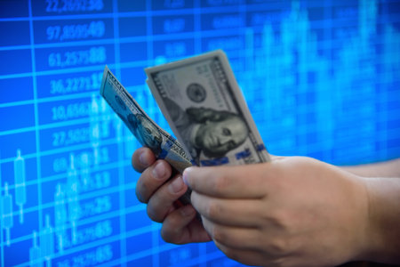 Businessman hands holding and counting dollar banknotes with a stock chart background, symbolizing...