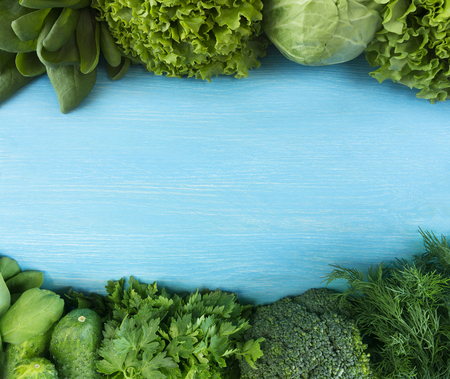 Green vegetables. Green vegetable on blue wooden background. Spinach, lettuce, cabbage, broccoli, cucumbers, parsley and dill. Top view. Vegetables at border of image with copy space for text.    の写真素材