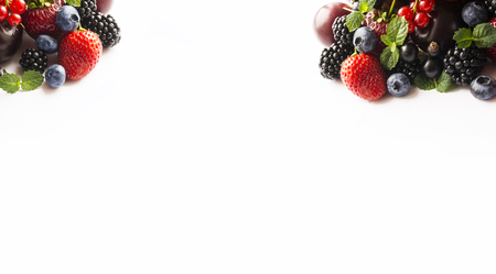 Mix berries and fruits at border of image with copy space for text. Black-blue and red food. Ripe blackberries, blueberries, strawberries, currants and mint leaves on a white background. Top view. Background berries. Various fresh summer berries. の写真素材
