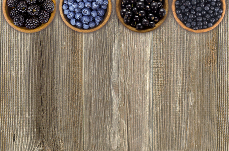 Black and blue berries. Blackberries, blueberries, currants and blueberries in a wooden bowls. Berries at border of image with copy space for text. Top view.の写真素材