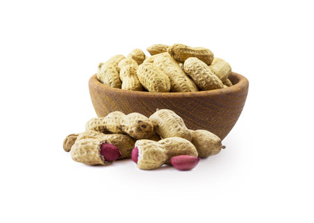 Studio shot of peanuts on white background. Peanuts in nutshell on wooden bowl isolated on white. Peanuts with copy space for text. Nuts close-up.の写真素材