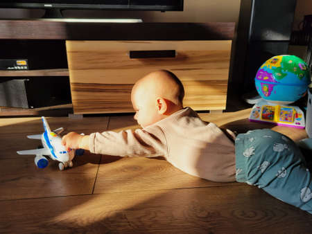Baby is playing with a toy plane on the floor in a room at sunsetの写真素材