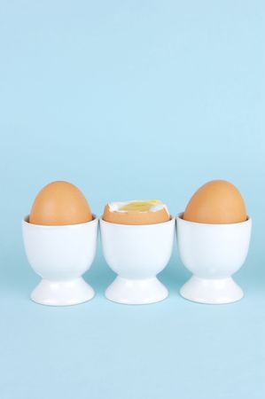 Hard boiled eggs and egg cups isolated against a blue backgroundの写真素材